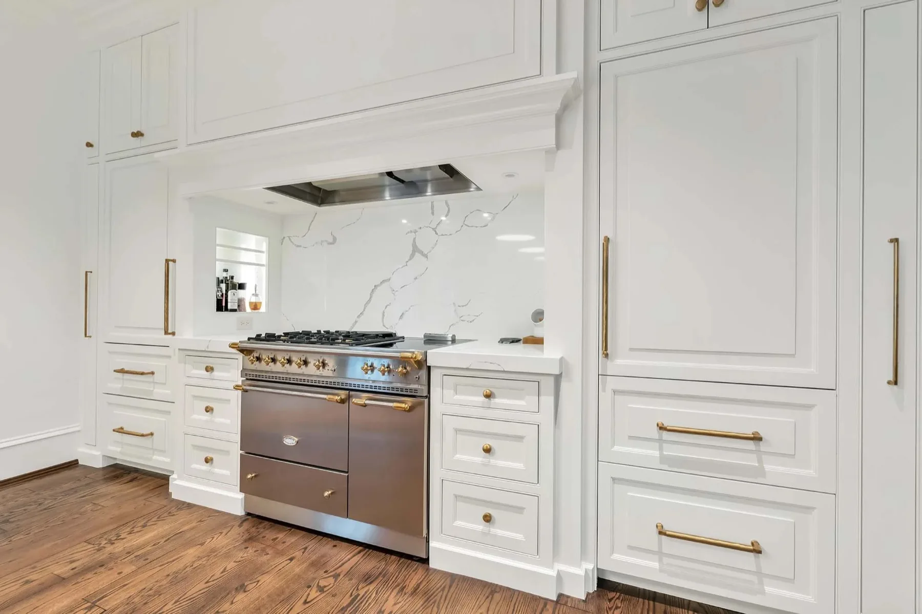 Custom painted kitchen cabinetry with brass hardware and a range alcove