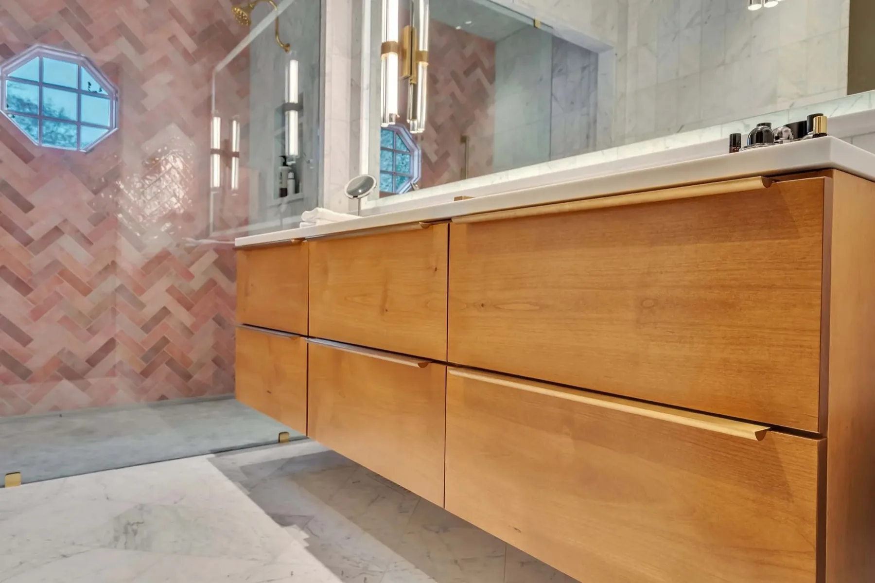Floating wood vanity with long brass pulls in a tiled bathroom